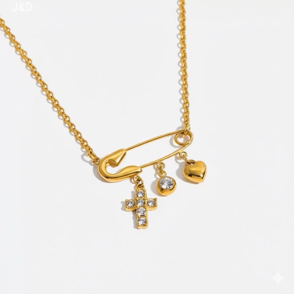 Gold necklace with safety pin, cross, and heart charms on a white background