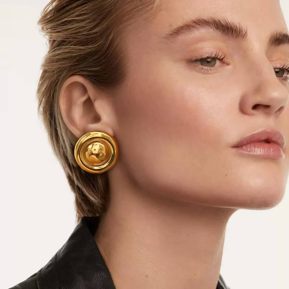 Close-up of a woman wearing gold earrings with a neutral background