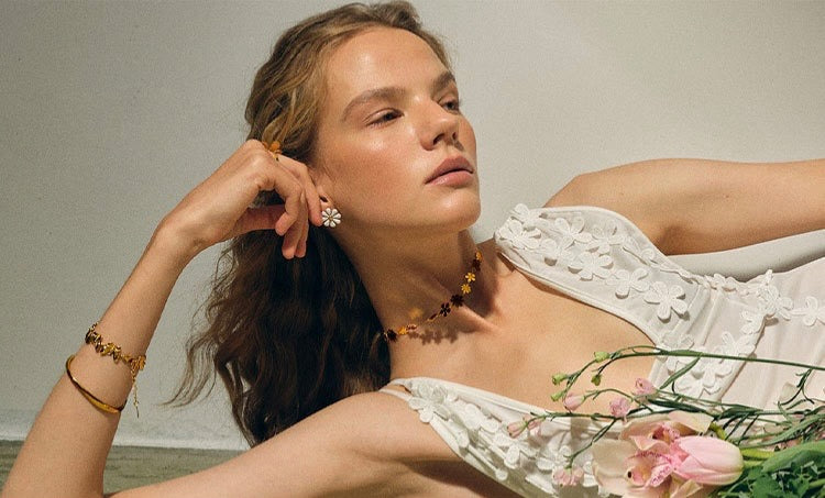 Woman in a white dress with floral details, holding flowers against a neutral background