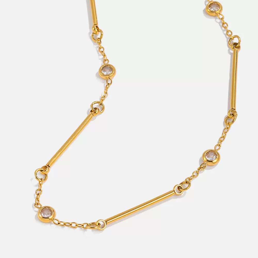 Gold necklace with small round stones on a light gray background