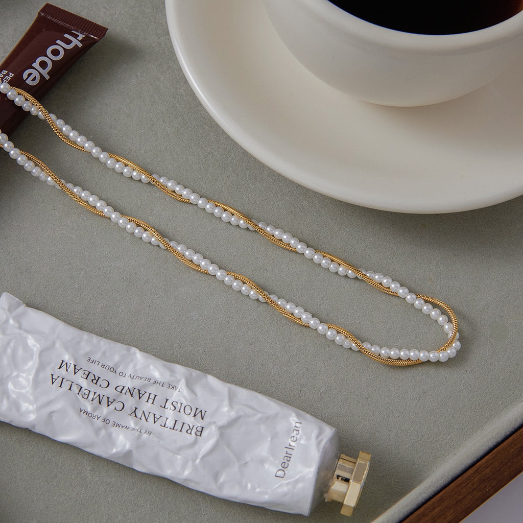 Pearl necklace on a surface with a cup of coffee and a tube of hand cream.
