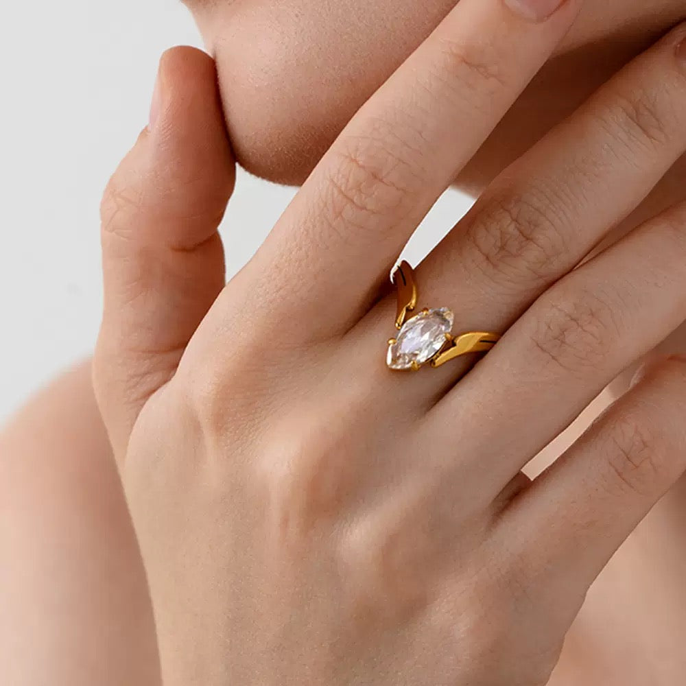 Gold ring with a clear gemstone on a hand against a neutral background