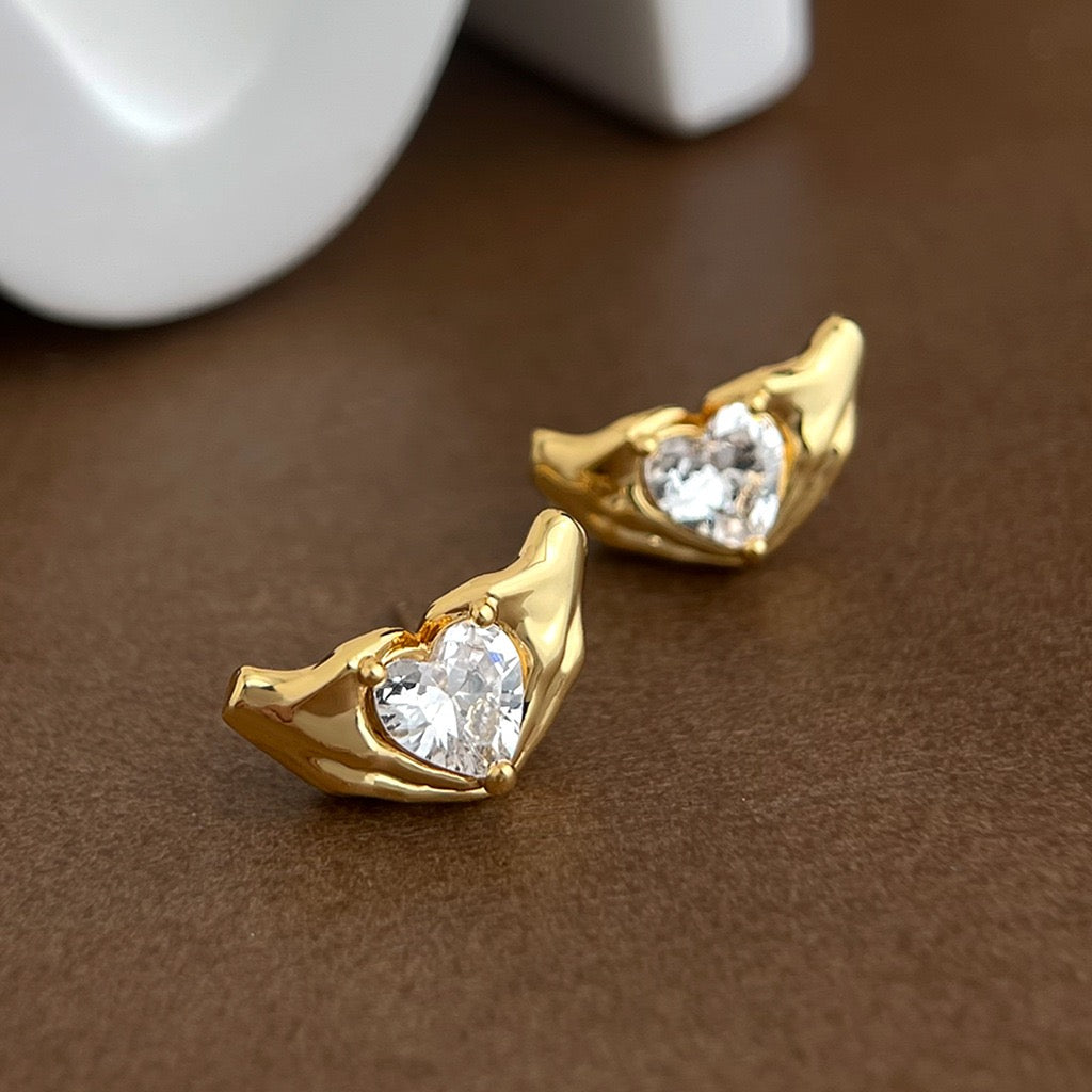 Gold earrings with heart-shaped gemstones on a brown surface