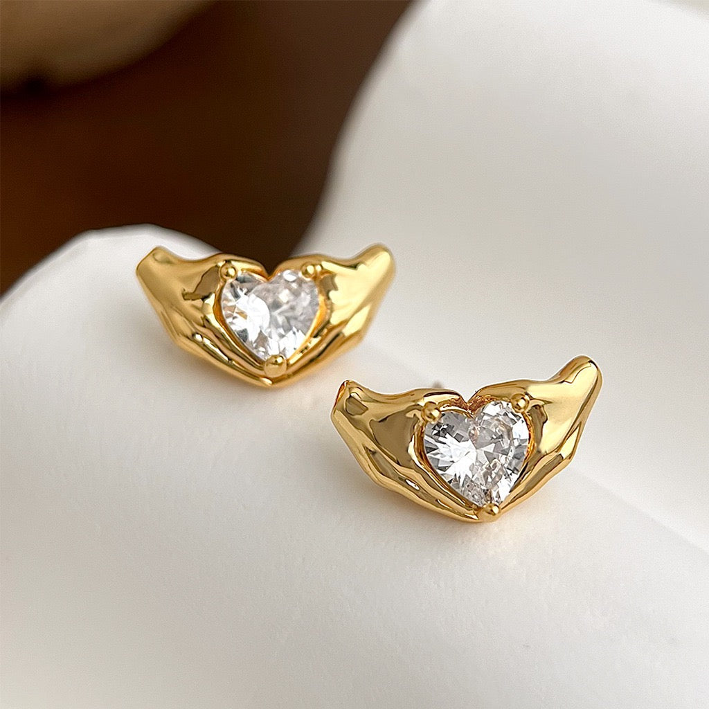 Gold heart-shaped earrings with clear cubic zirconia stones  on a white surface
