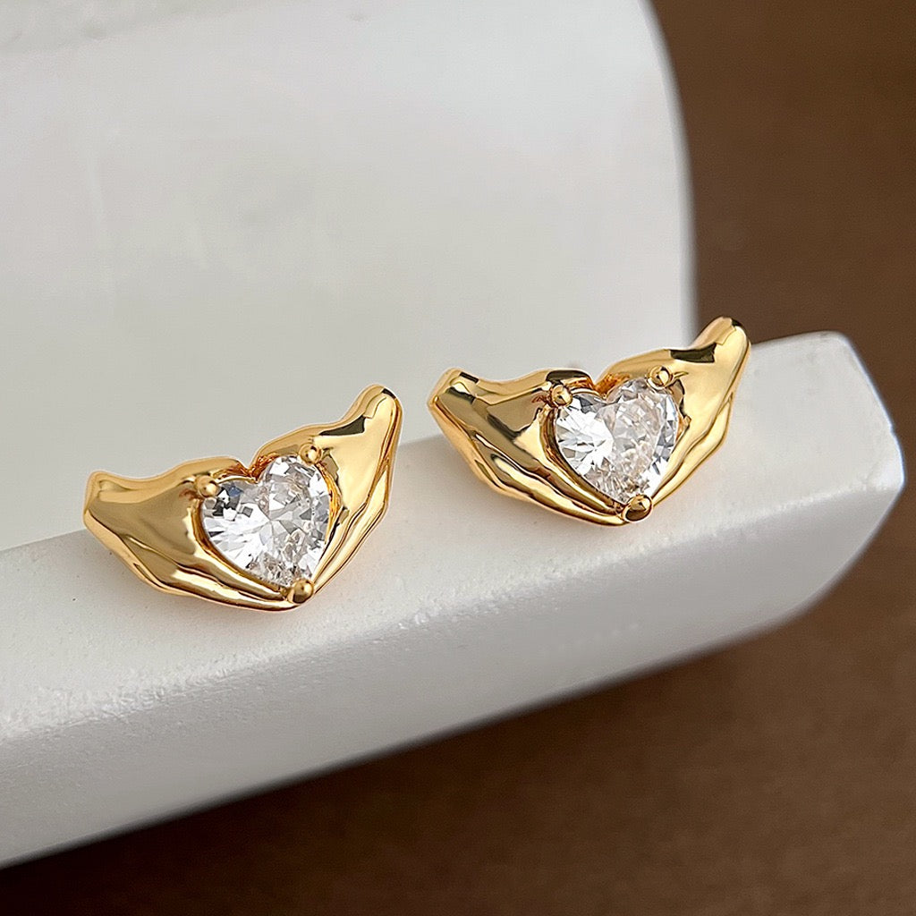 Gold heart-shaped earrings with clear gemstones on a white surface