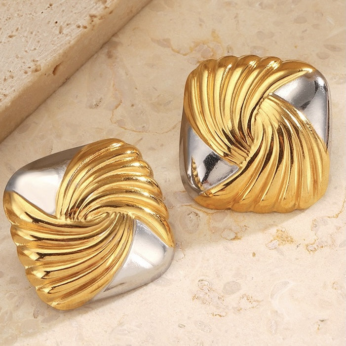 Pair of gold and silver spiral earrings on a beige stone surface