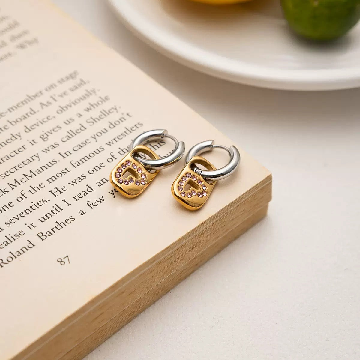 Pair of gold and silver earrings on an open book with a plate and lime in the background.