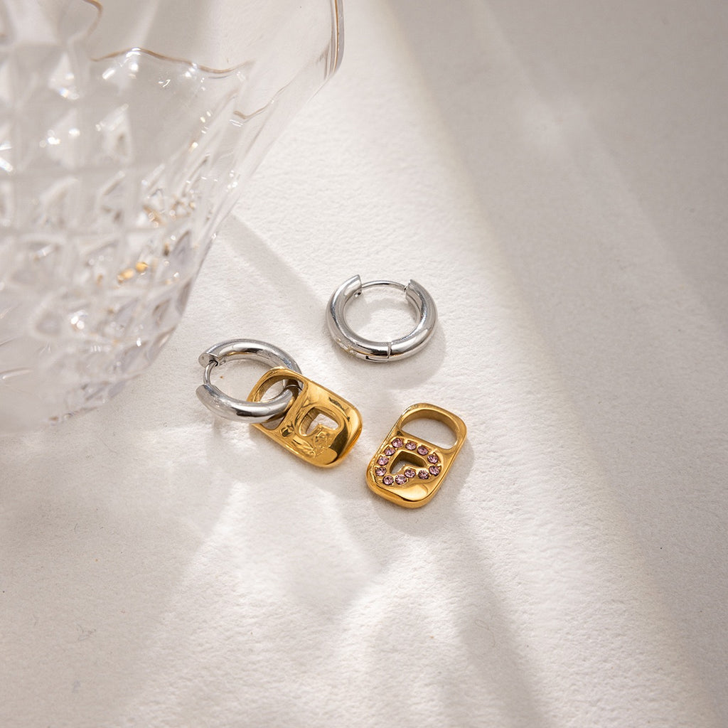 Pair of gold and silver hoop earrings on a textured white surface.