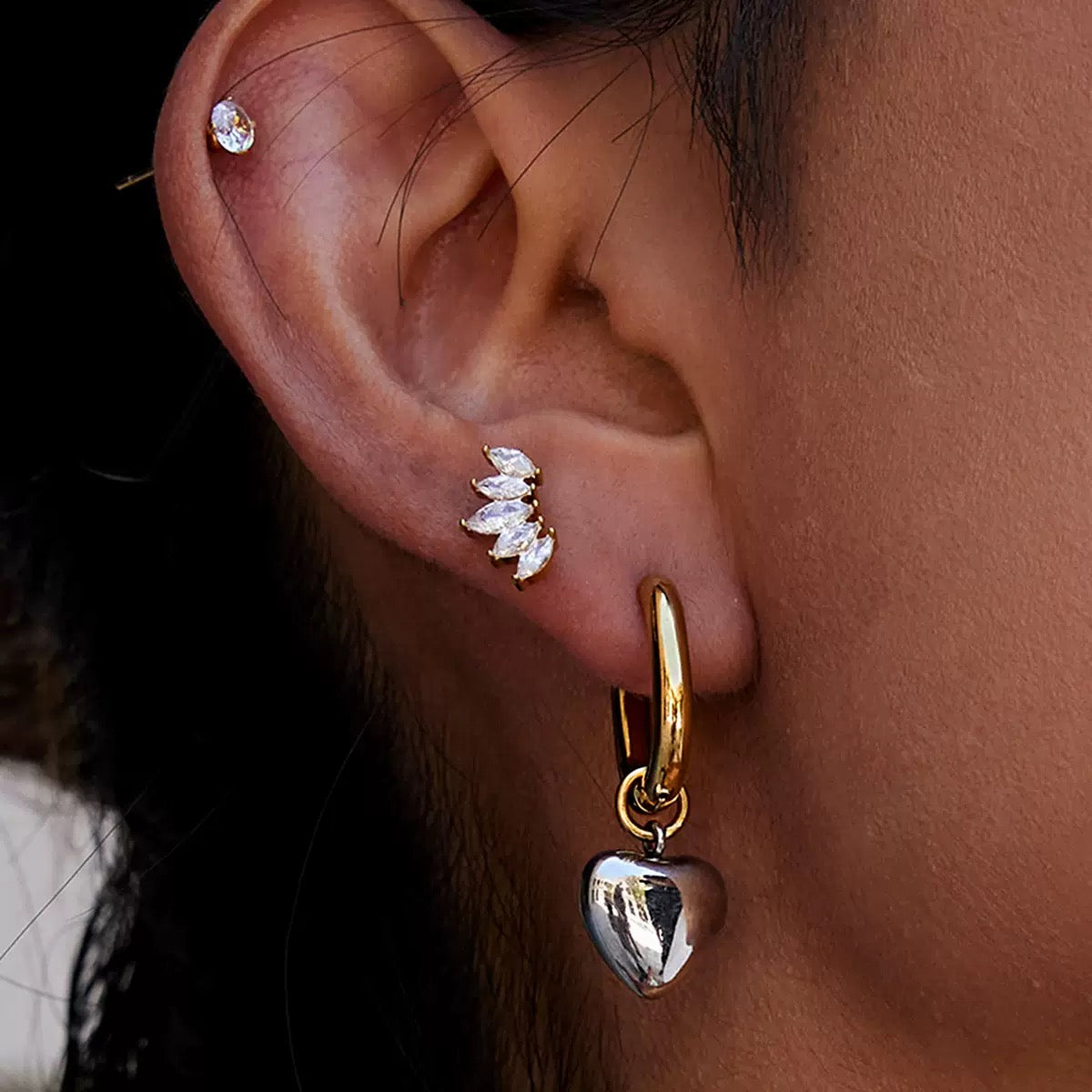 Close-up of an ear wearing gold hoop earrings with a heart charm and diamond-studded earrings.