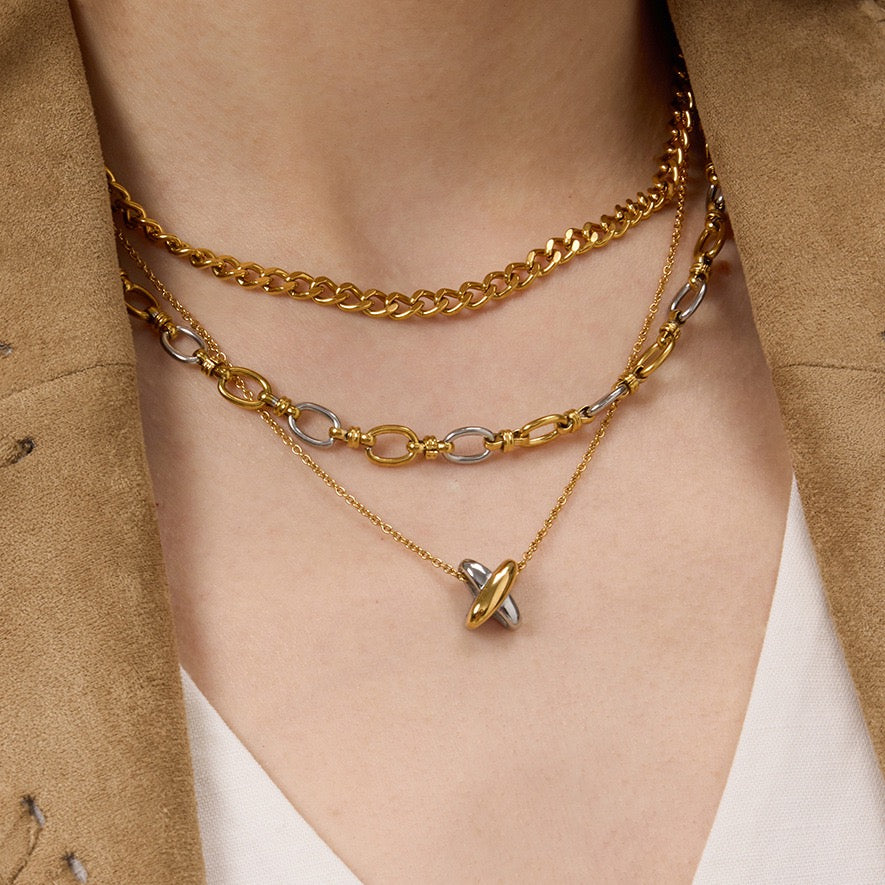 Layered gold necklaces on a person wearing a beige jacket.