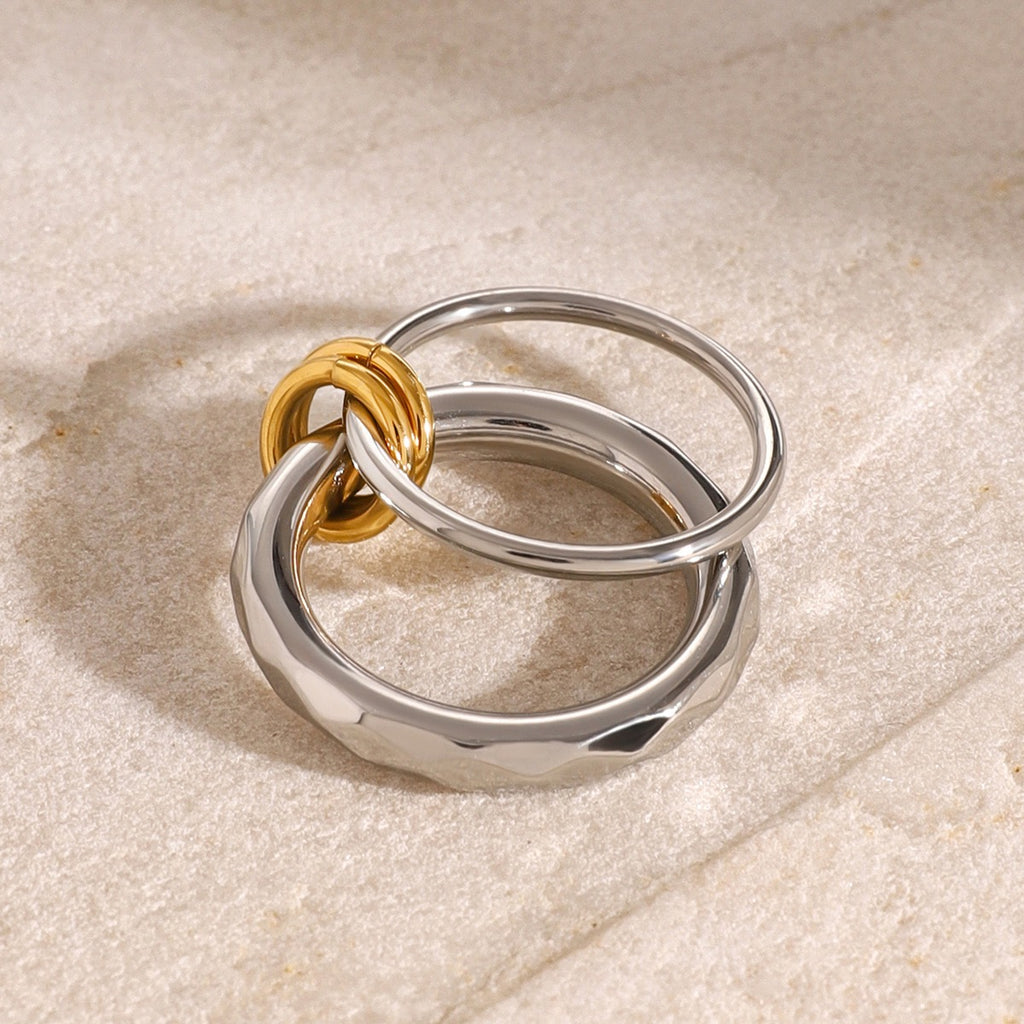 Two rings, one gold and one silver, stacked on a textured beige surface.