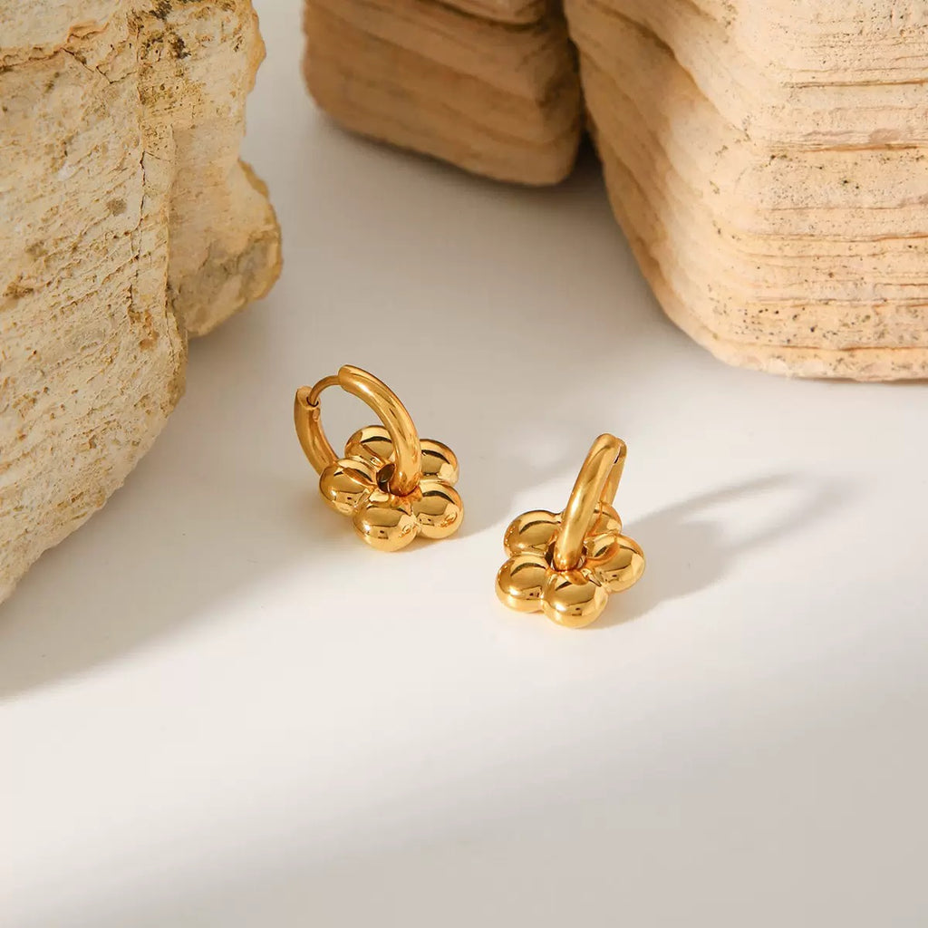 Gold earrings on a light surface with stone-like textures in the background