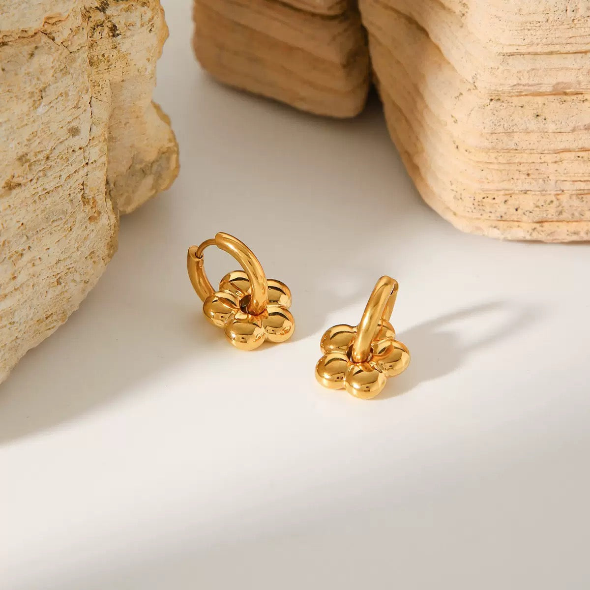 Gold earrings on a light surface with stone-like textures in the background