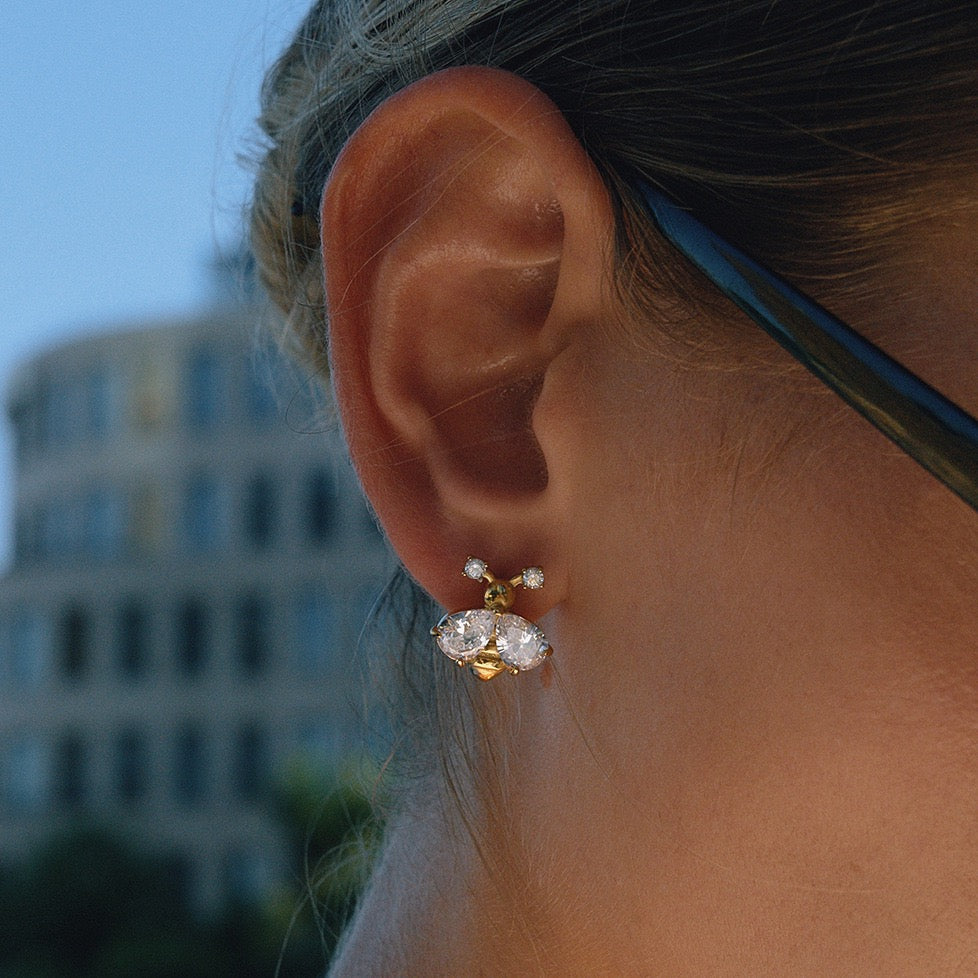 Close-up of an ear wearing a diamond earring with a blurred building in the background