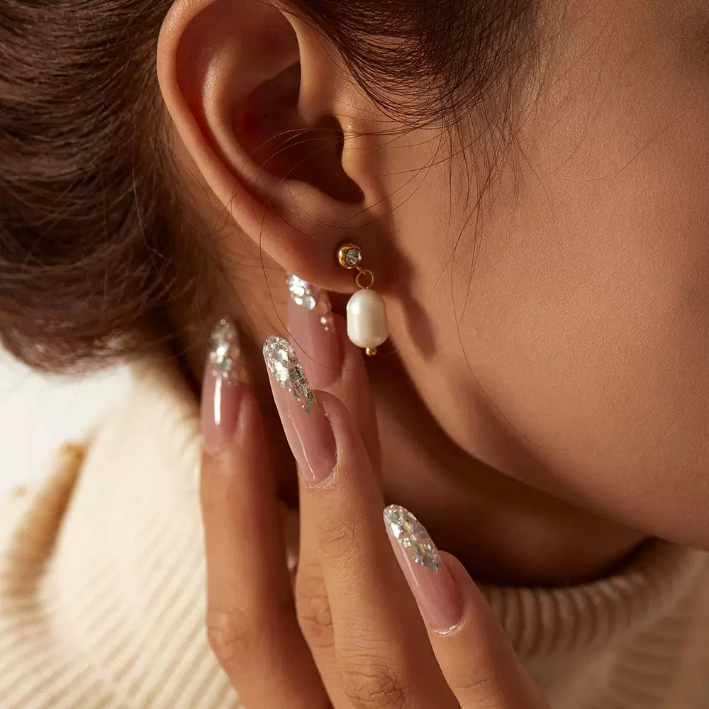 Close-up of an ear wearing pearl and crystal earrings with a hand touching the ear.