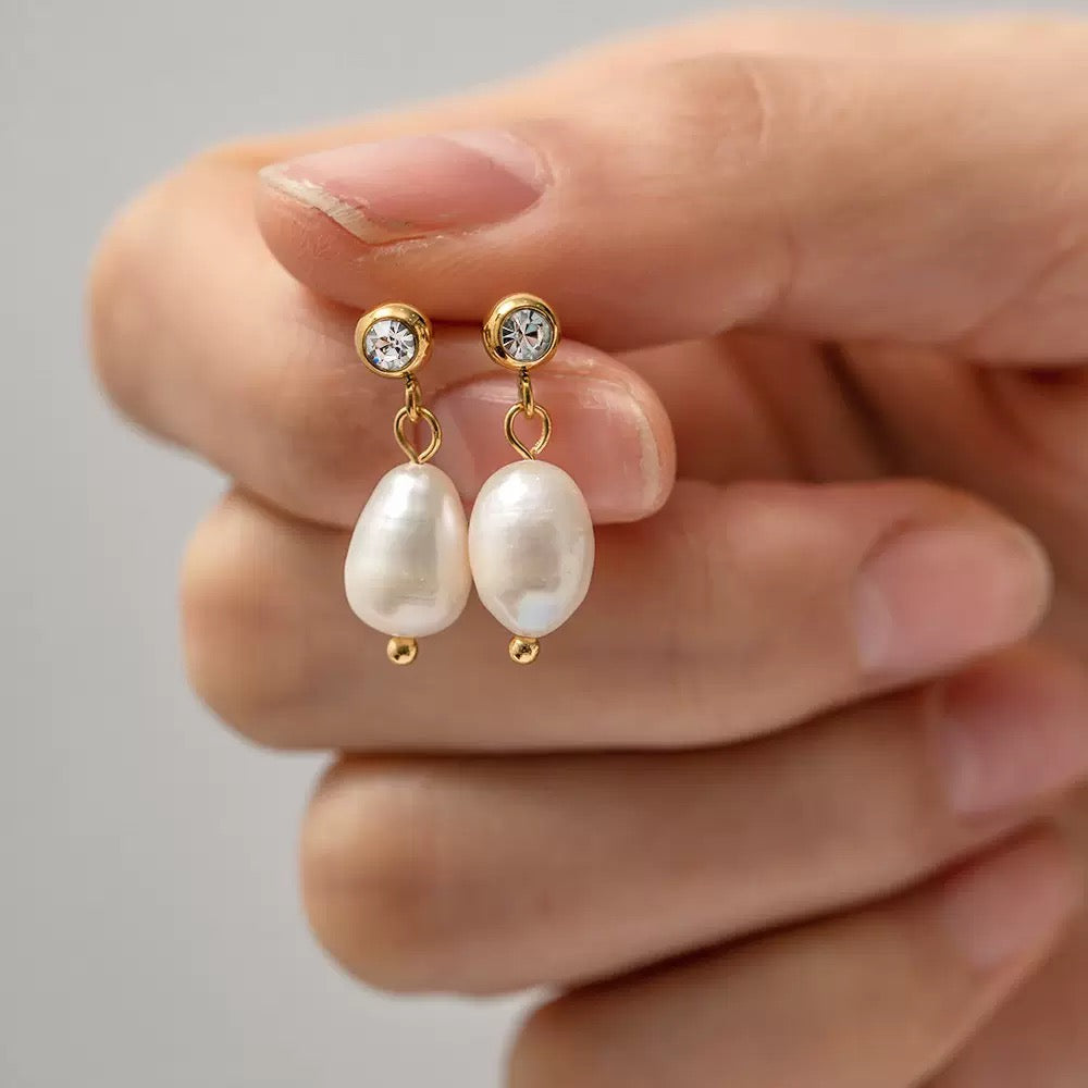 Pearl earrings with gold accents held between fingers against a neutral background