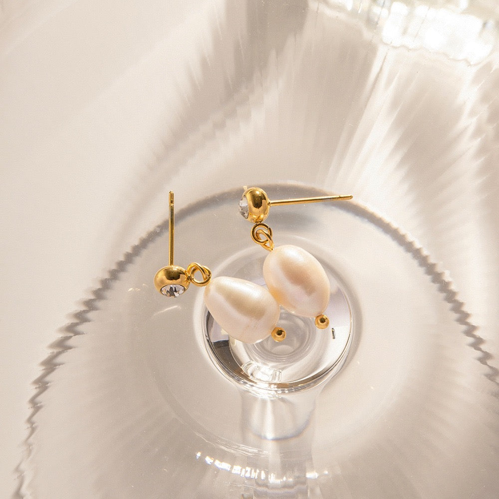 Pearl earrings with gold accents on a reflective surface