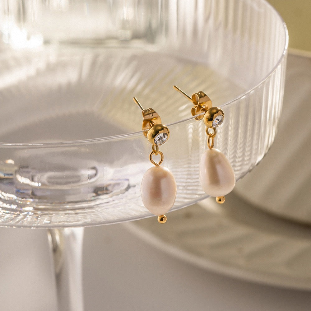 Pearl earrings with gold accents on a clear stand