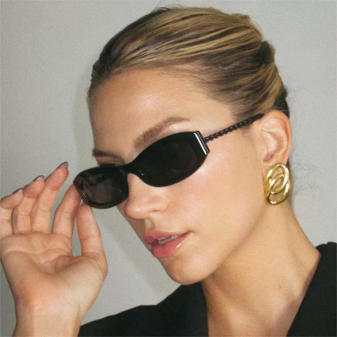 Woman wearing black sunglasses and gold earrings against a neutral background