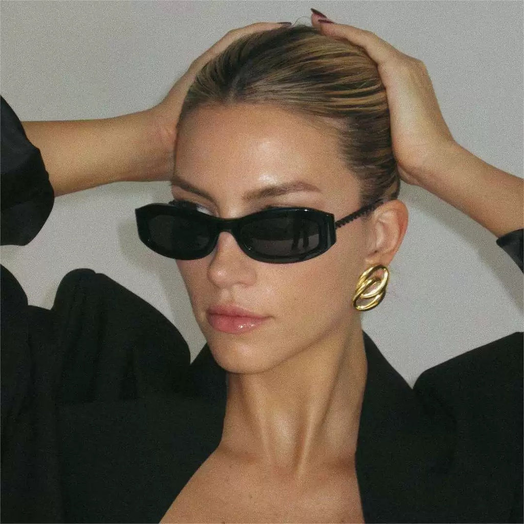 Woman wearing black sunglasses and gold earrings with a plain background