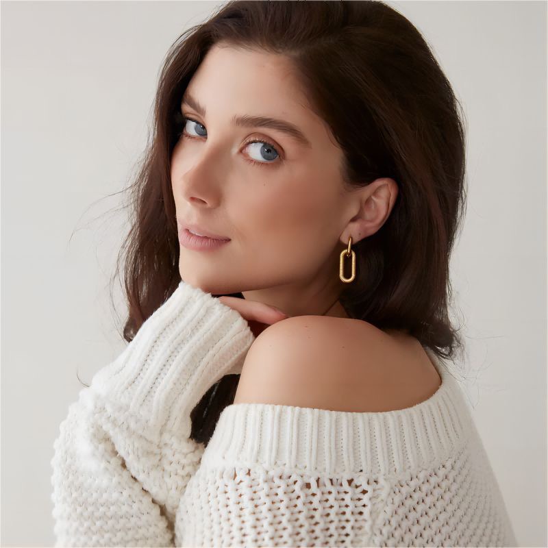 Woman wearing a white sweater and gold earrings against a plain background
