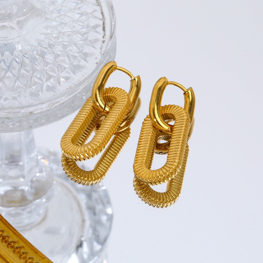 Gold hoop earrings on a white surface with a glass of water in the background