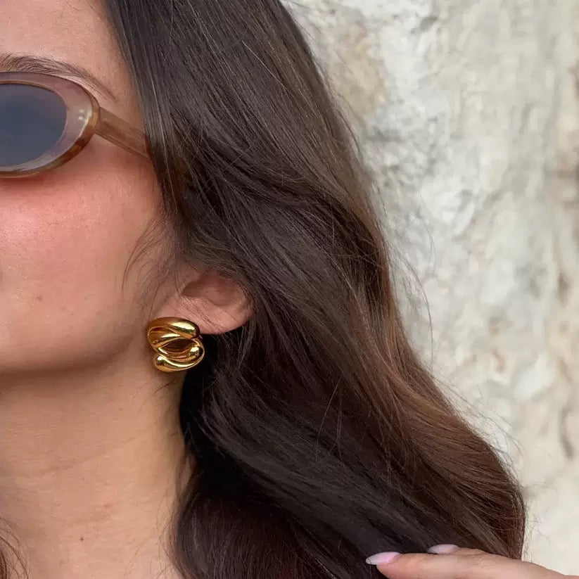Close-up of a person wearing gold hoop earrings with a neutral background