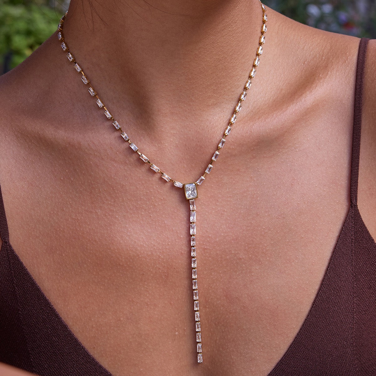 Necklace with a central gemstone on a person wearing a brown top.