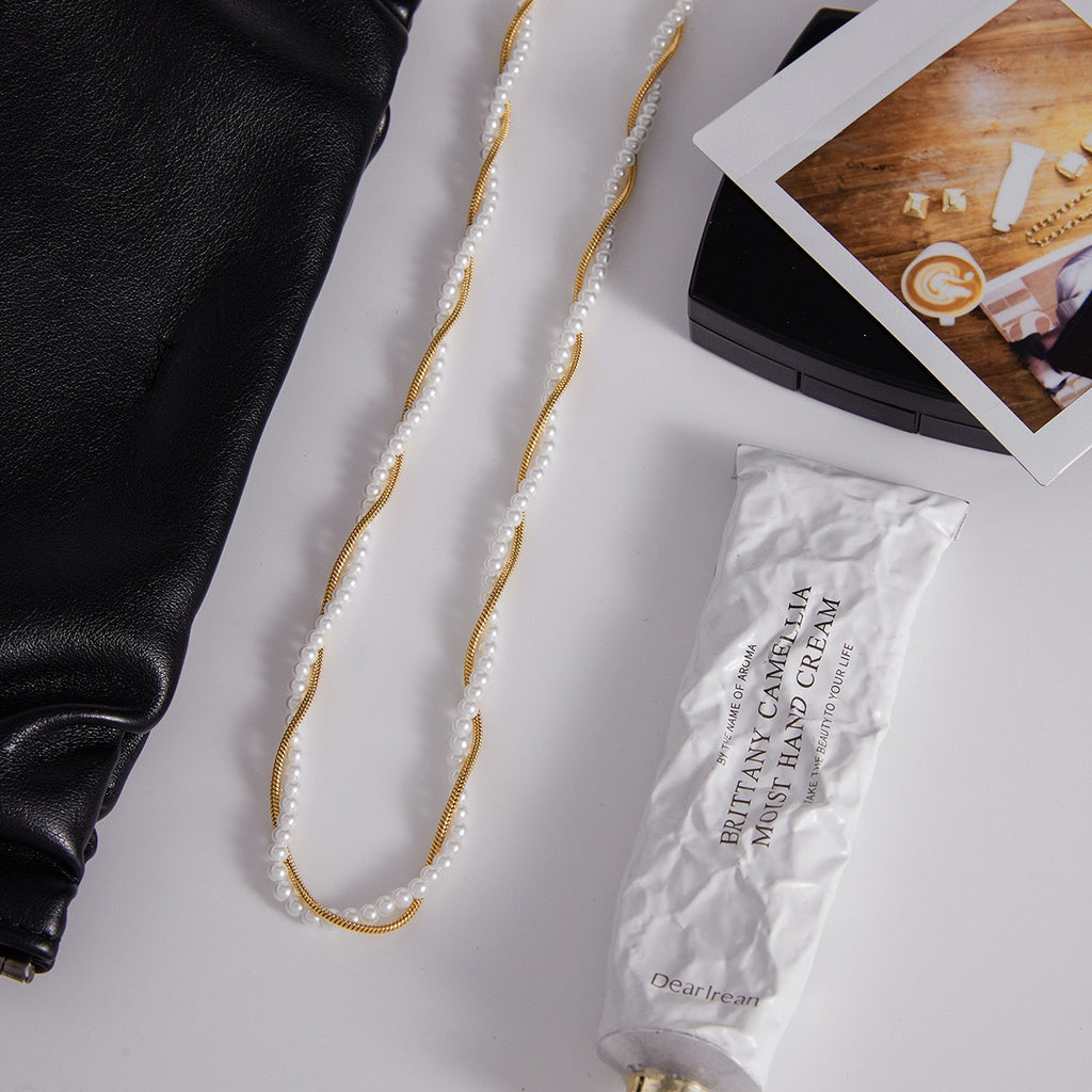 Pearl necklace, black handbag, and white hand cream on a light gray surface