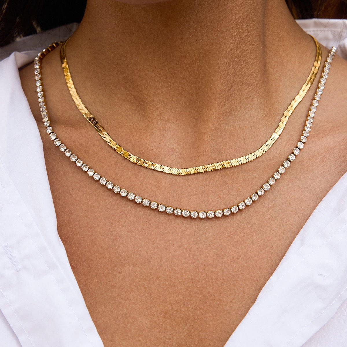Two gold necklaces on a person wearing a white top.