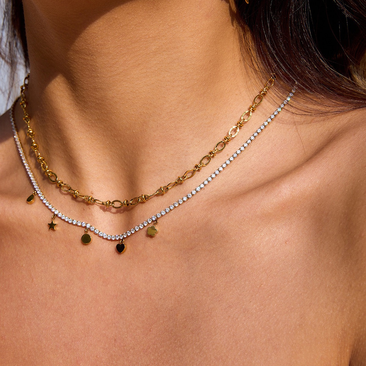 Close-up of a person wearing two gold necklaces with star and round pendants.