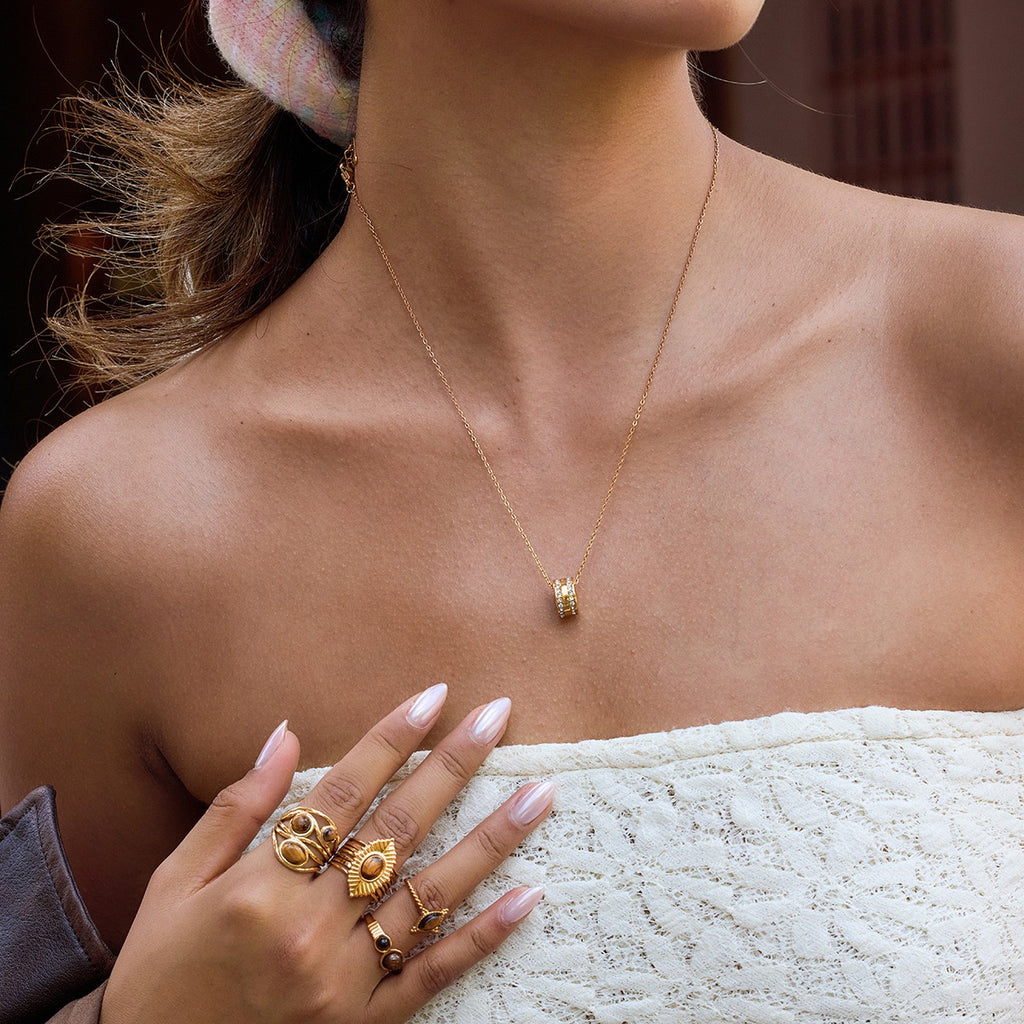 Close-up of a person wearing gold jewelry including a necklace, rings, and earrings.
