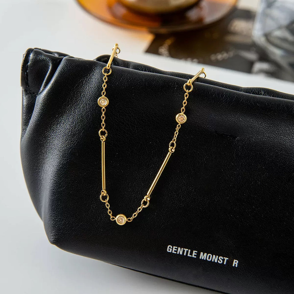 Gold necklace on a black Gentle Monster pouch with a blurred background