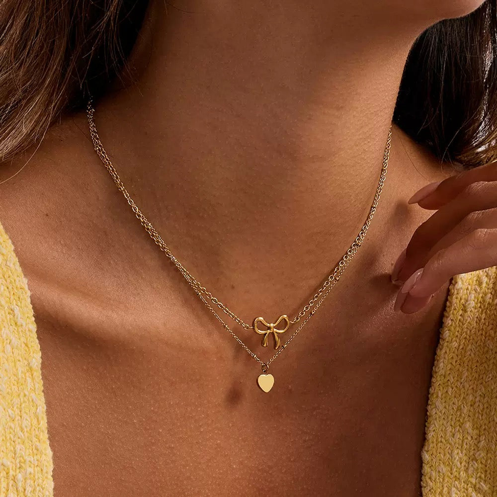 Gold necklace with bow and heart pendant on a person wearing a yellow top.