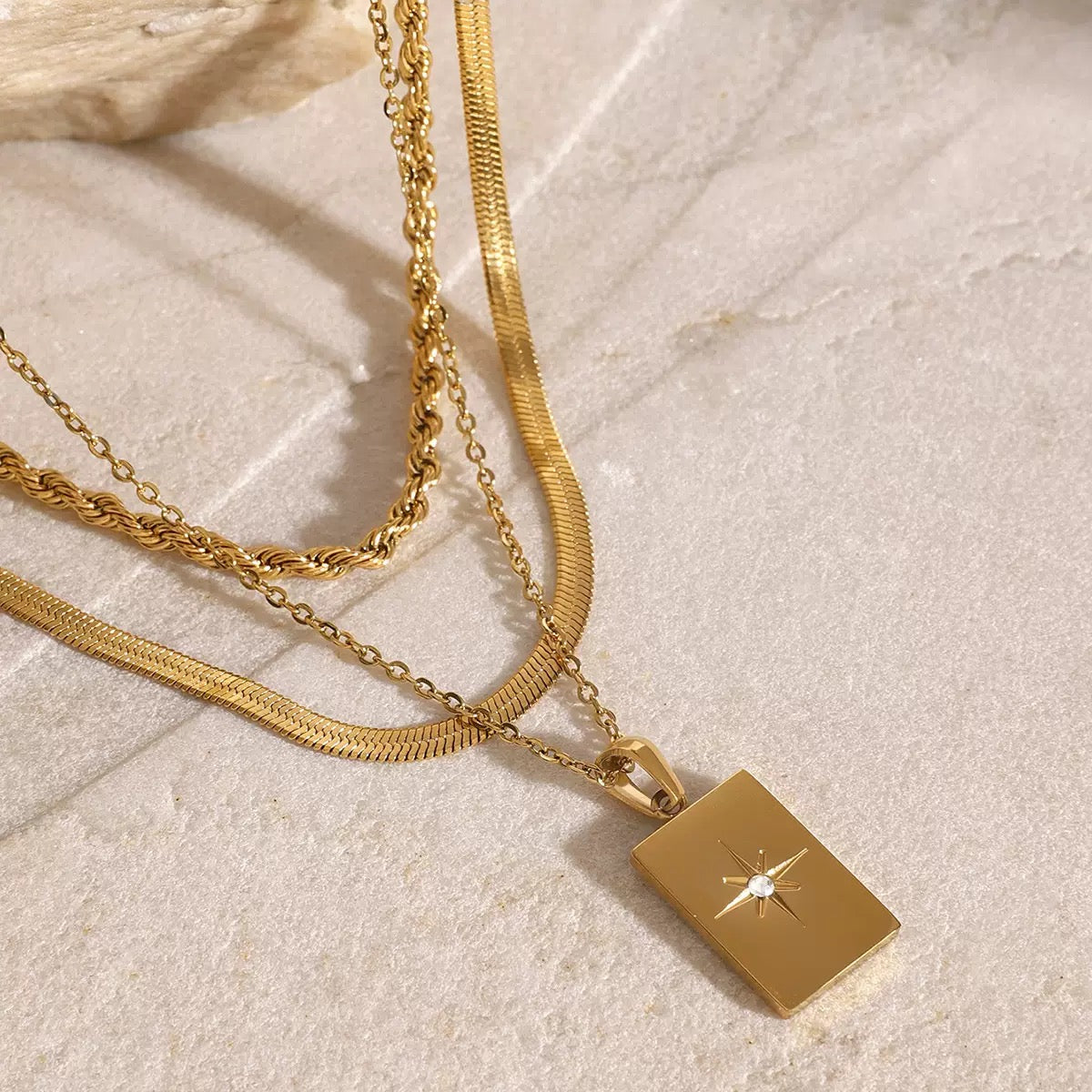 Gold necklace with a square pendant on a light stone surface