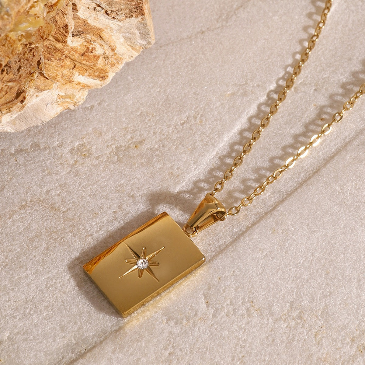 Gold necklace with a pendant on a textured beige surface