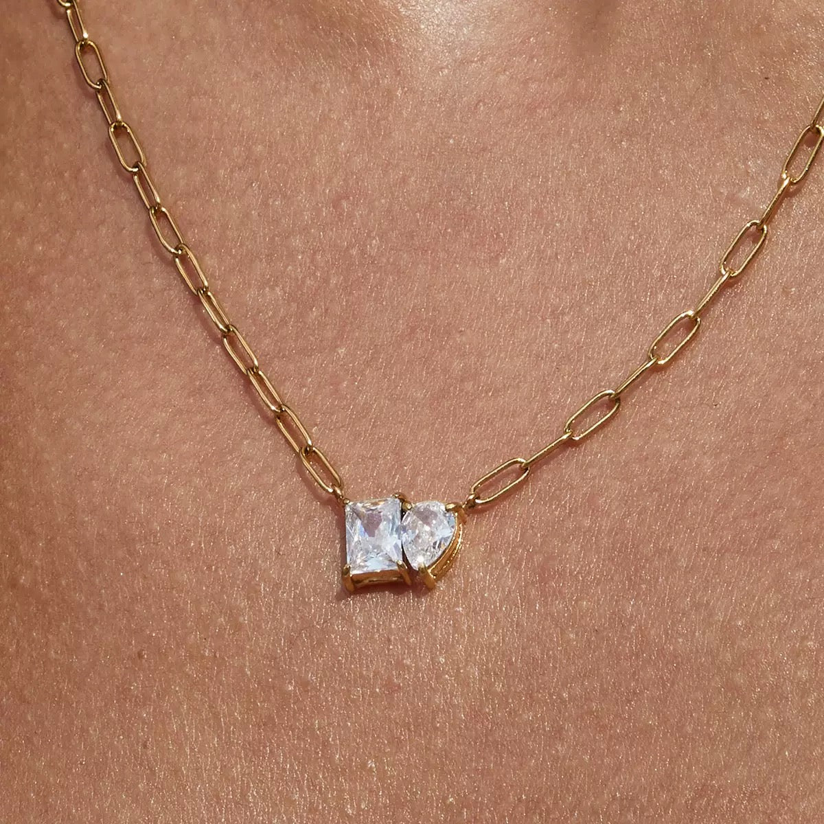 Gold necklace with a heart-shaped diamond pendant on a skin background
