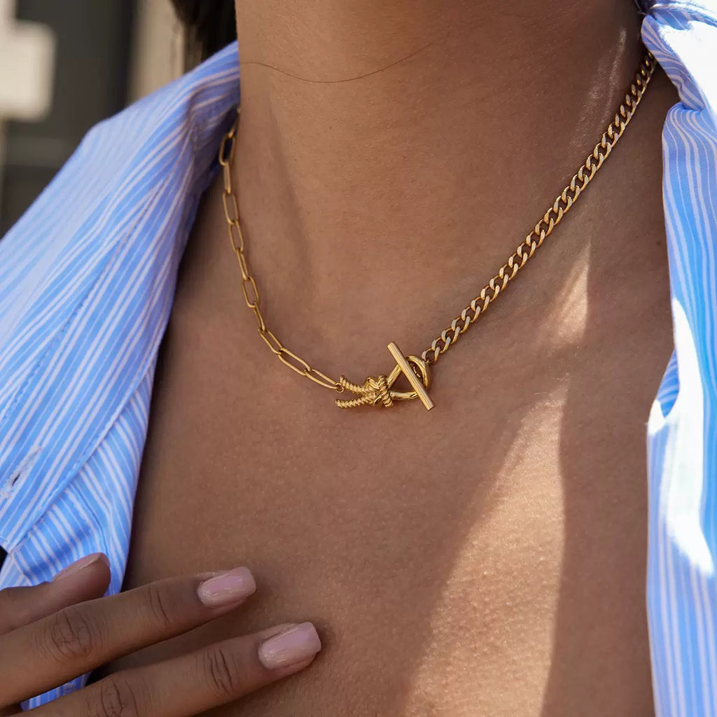 Gold chain necklace with a unique clasp worn by a person against a blurred background