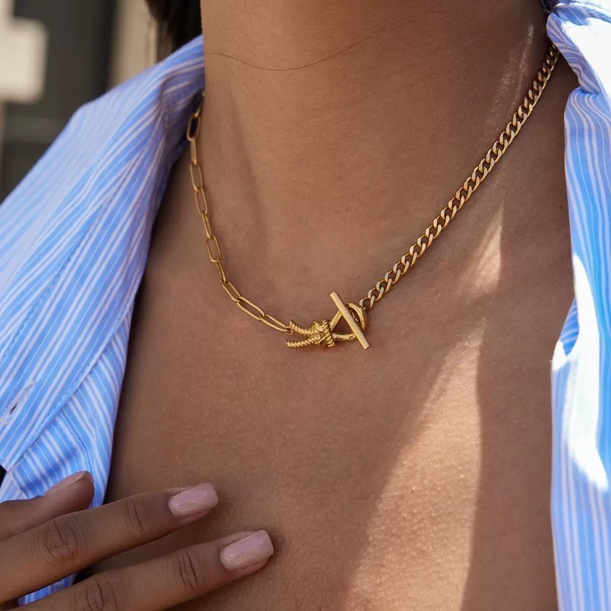 Gold chain necklace with a unique clasp worn by a person against a blurred background