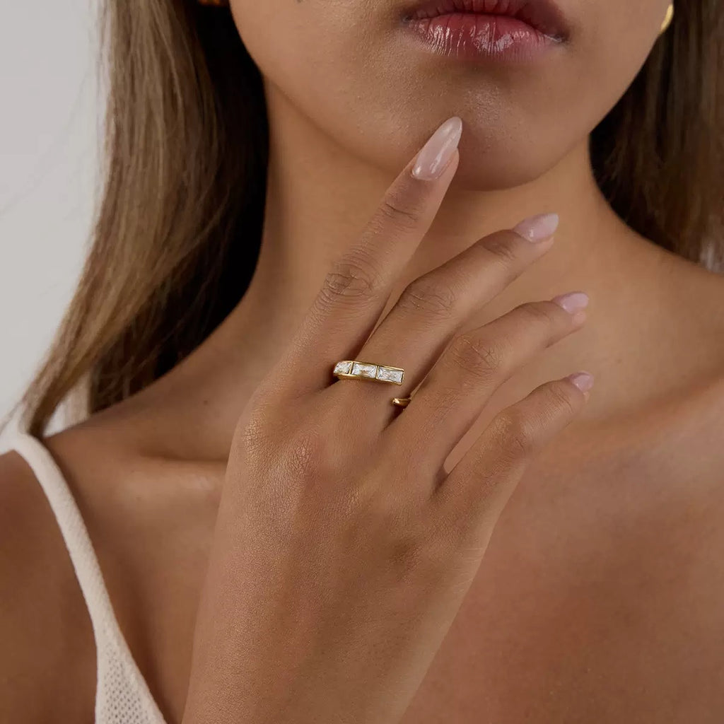 Close-up of a woman's hand wearing a gold ring with a diamond, touching her neck.