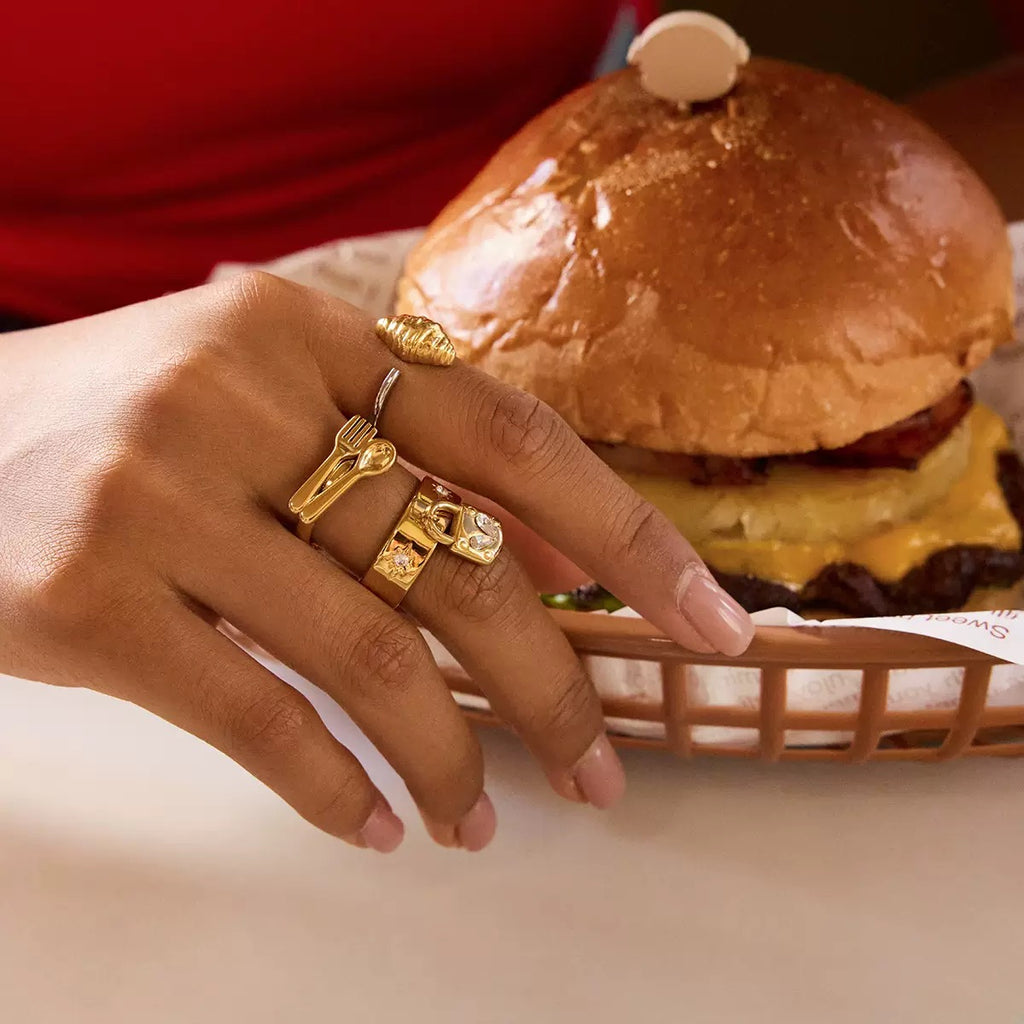 Hand with gold rings holding a burger in a basket