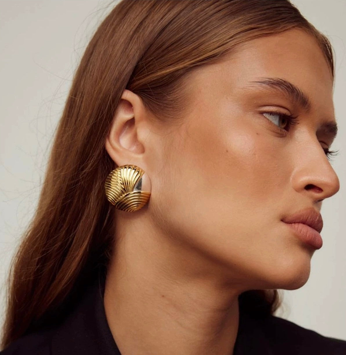Close-up of a woman wearing gold earrings with a neutral background