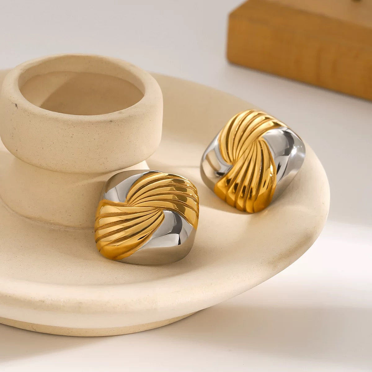 Gold and silver earrings on a beige stone surface with a wooden block in the background