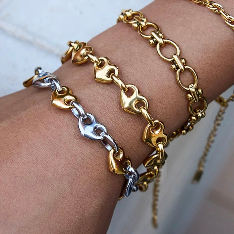 Gold and silver chain bracelets on a wrist against a neutral background