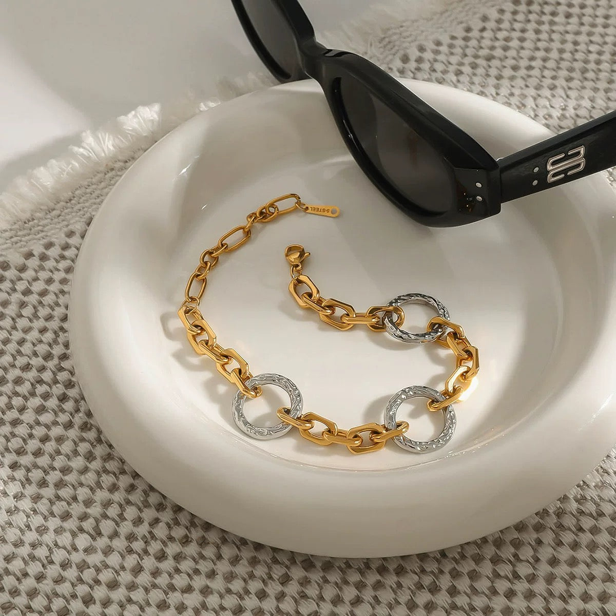 Gold and silver chain bracelet on a white dish with black sunglasses