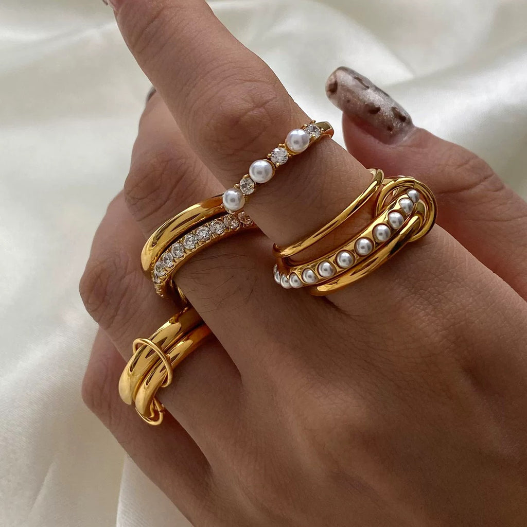 Hand wearing three gold rings with pearl accents on a white background