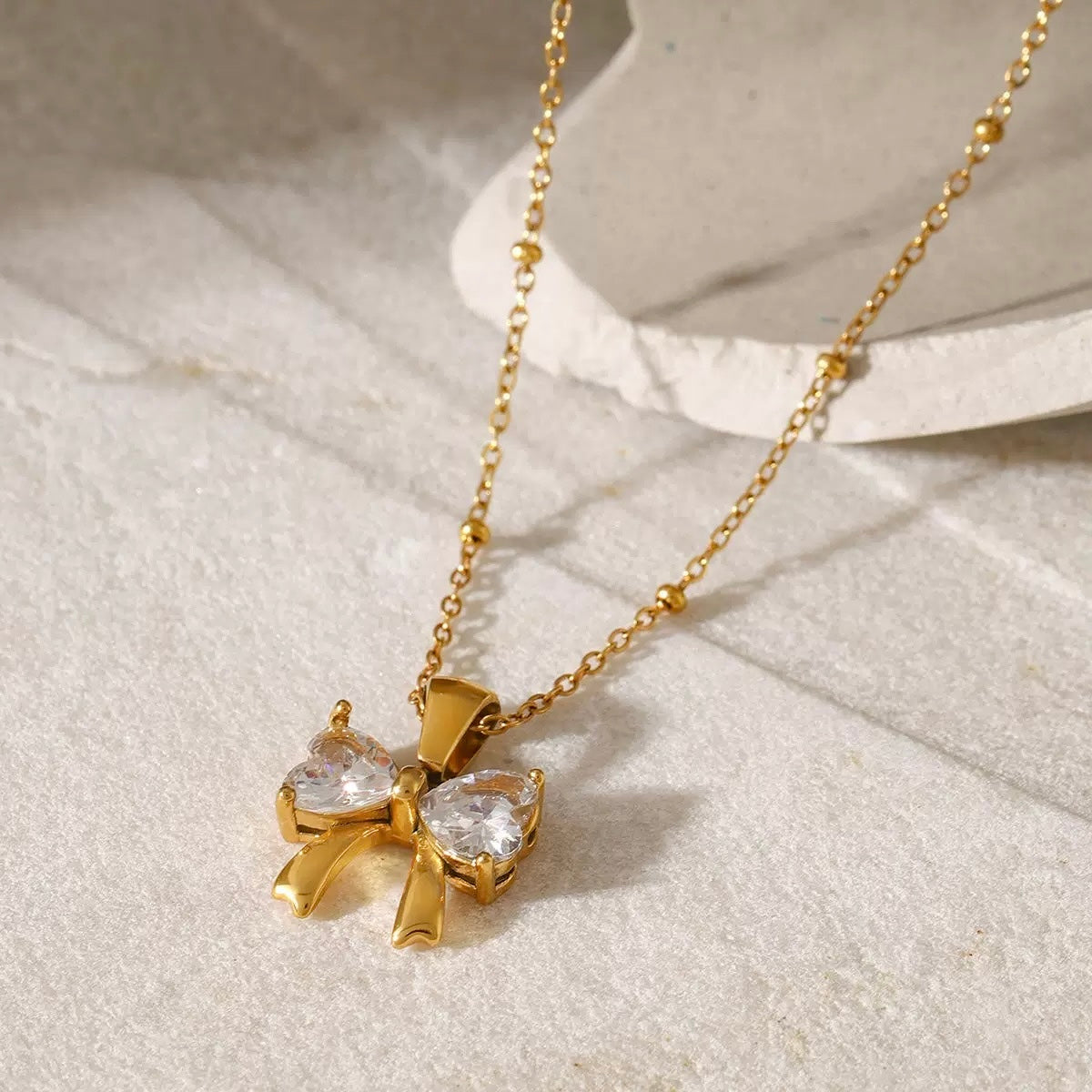 Gold necklace with a bow-shaped pendant on a light background