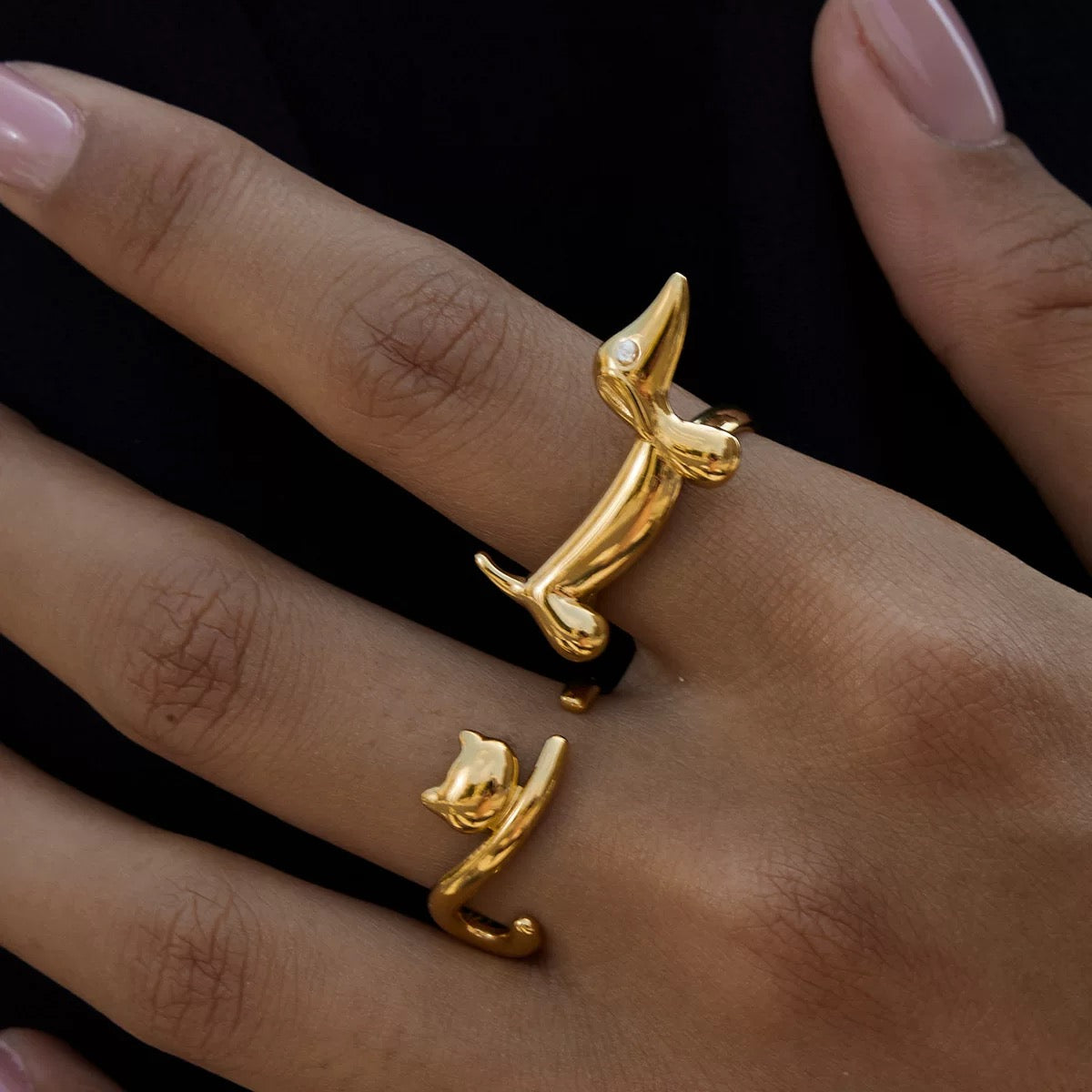 Gold dog-shaped ring on a hand against a black background