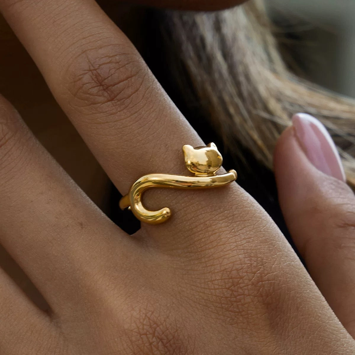 Gold cat-shaped ring on a person's finger