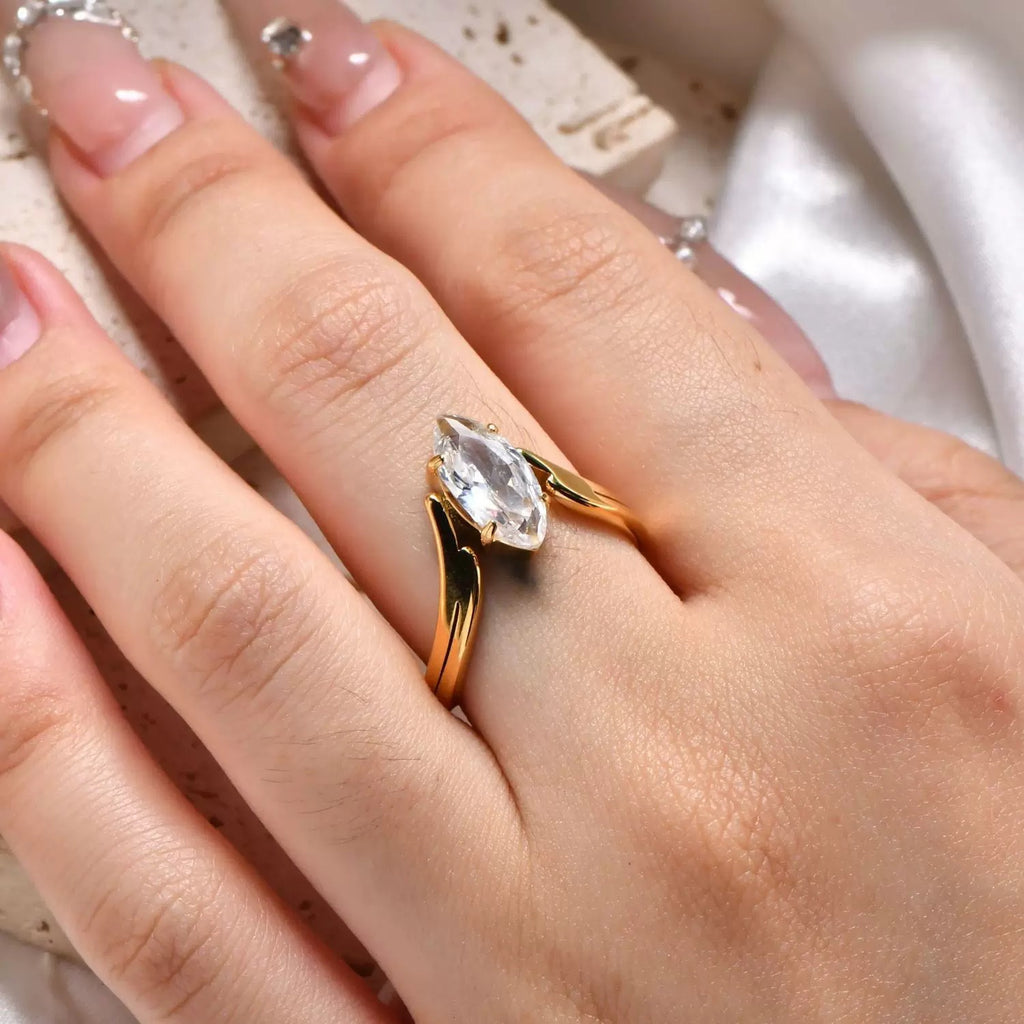 Gold ring with a pear-shaped diamond on a hand against a neutral background